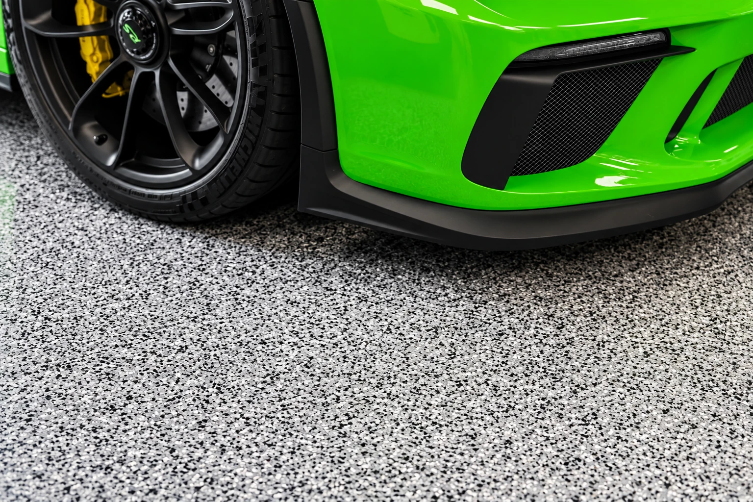 Close view of a bright green sports car over a light gray, black, and white flake-coated concrete floor.