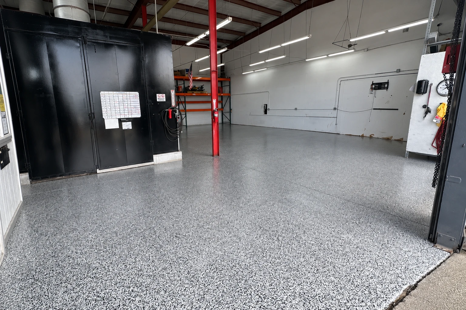Gray speckled epoxy coating covers an empty industrial workshop floor beneath fluorescent lights.