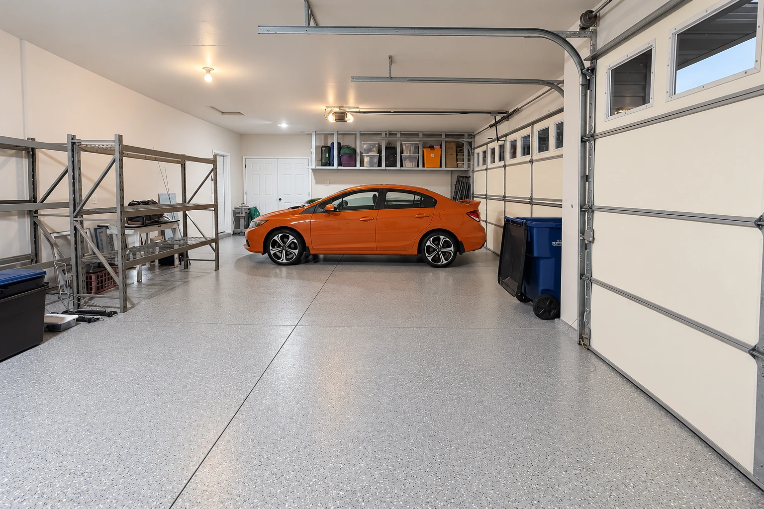 Light gray epoxy-coated garage floor with a speckled finish beneath an orange car and storage shelves.