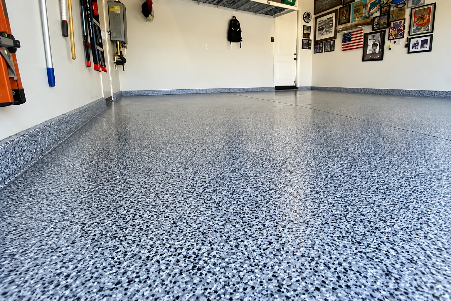 A clean garage with a glossy gray flake epoxy floor, wall-mounted tools, and framed pictures beside a door.