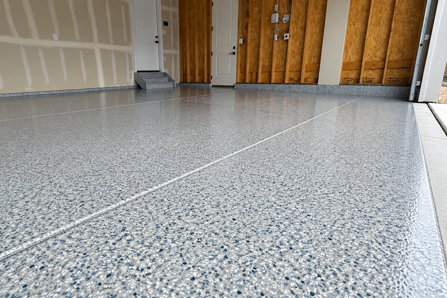 Speckled gray epoxy floor fills a garage with unfinished walls and visible floor seams.