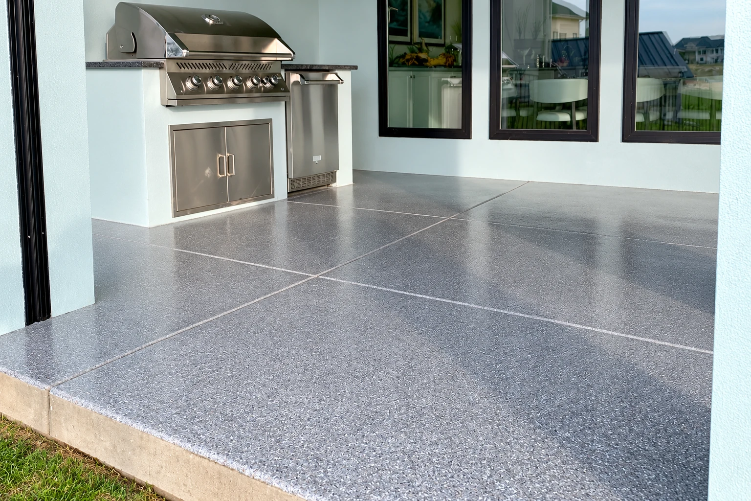 Gray speckled concrete patio with scored joints beside an outdoor kitchen and grill.