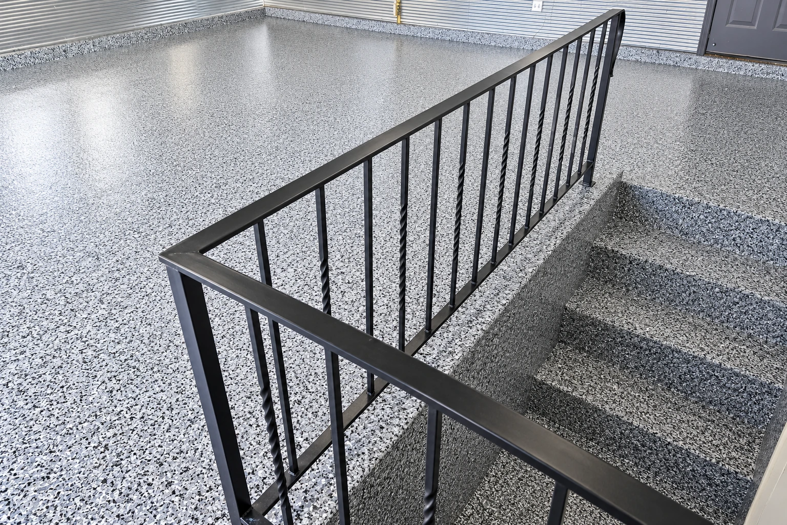 Gray-and-white flake-coated concrete covers a sunken garage area beside a black metal railing.