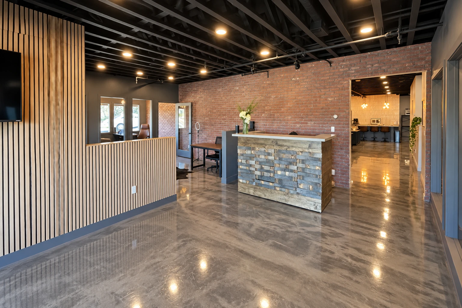 Polished concrete flooring reflects warm ceiling lights in a reception area with brick walls and a wood-slat divider.
