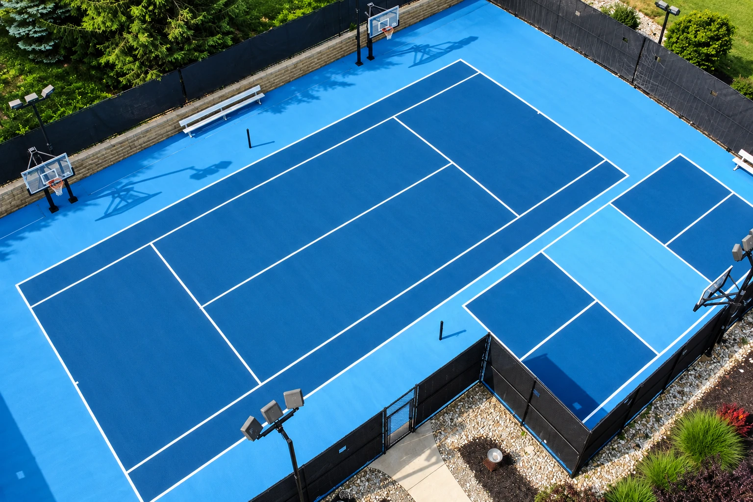 An aerial view of a bright blue outdoor basketball court shows dark blue playing areas and crisp white lines.
