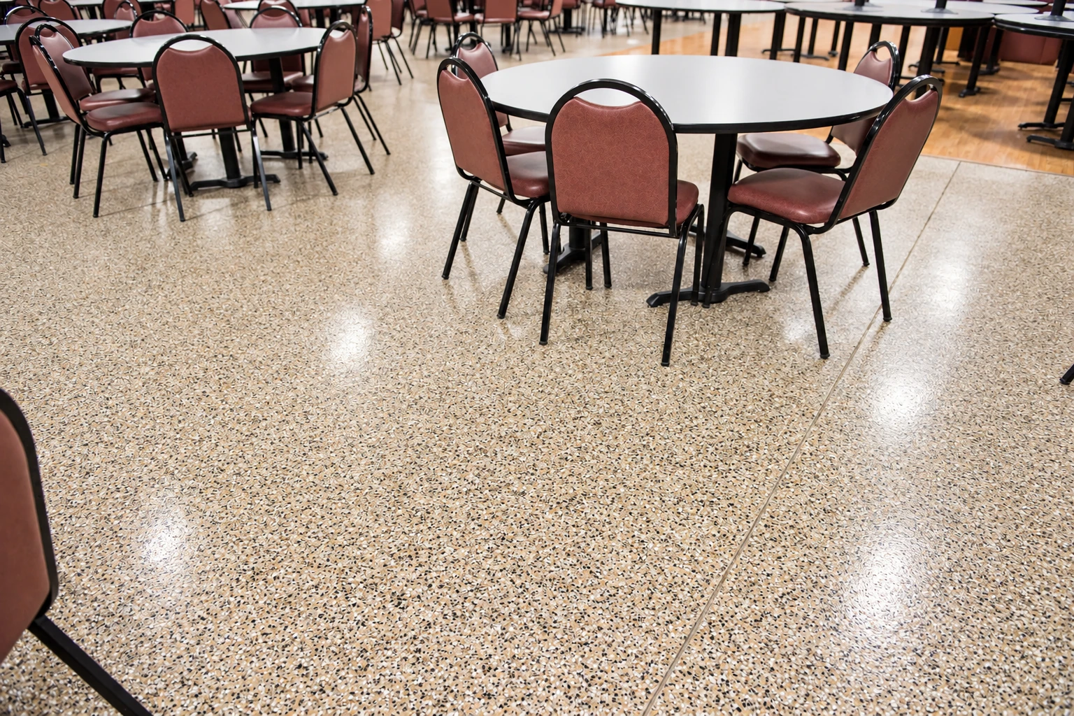 Polished terrazzo floor with cream, tan, and dark chips in a dining room furnished with round tables and chairs.